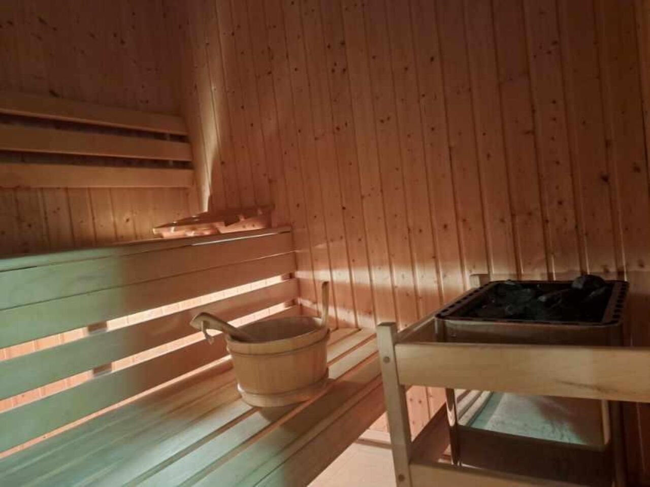 Un sauna en bois avec des bancs et une table, un seau en bois et un poêle.