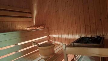 Un sauna en bois avec des bancs et une table, un seau en bois et un poêle.