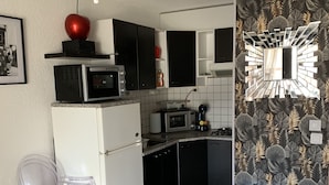 Eine kleine Küche mit Mikrowelle, Toaster und Kaffeemaschine. Es gibt einen weißen Kühlschrank, eine schwarze Arbeitsplatte und einen klaren Kunststoffstuhl.