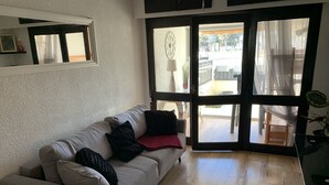 Ein Wohnzimmer mit einer Couch, einer Tür zu einem Außenbereich und einem Blumentopf.