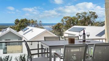 A terrace with a table and chairs, solar panels on the roof, and a view of the ocean and trees.