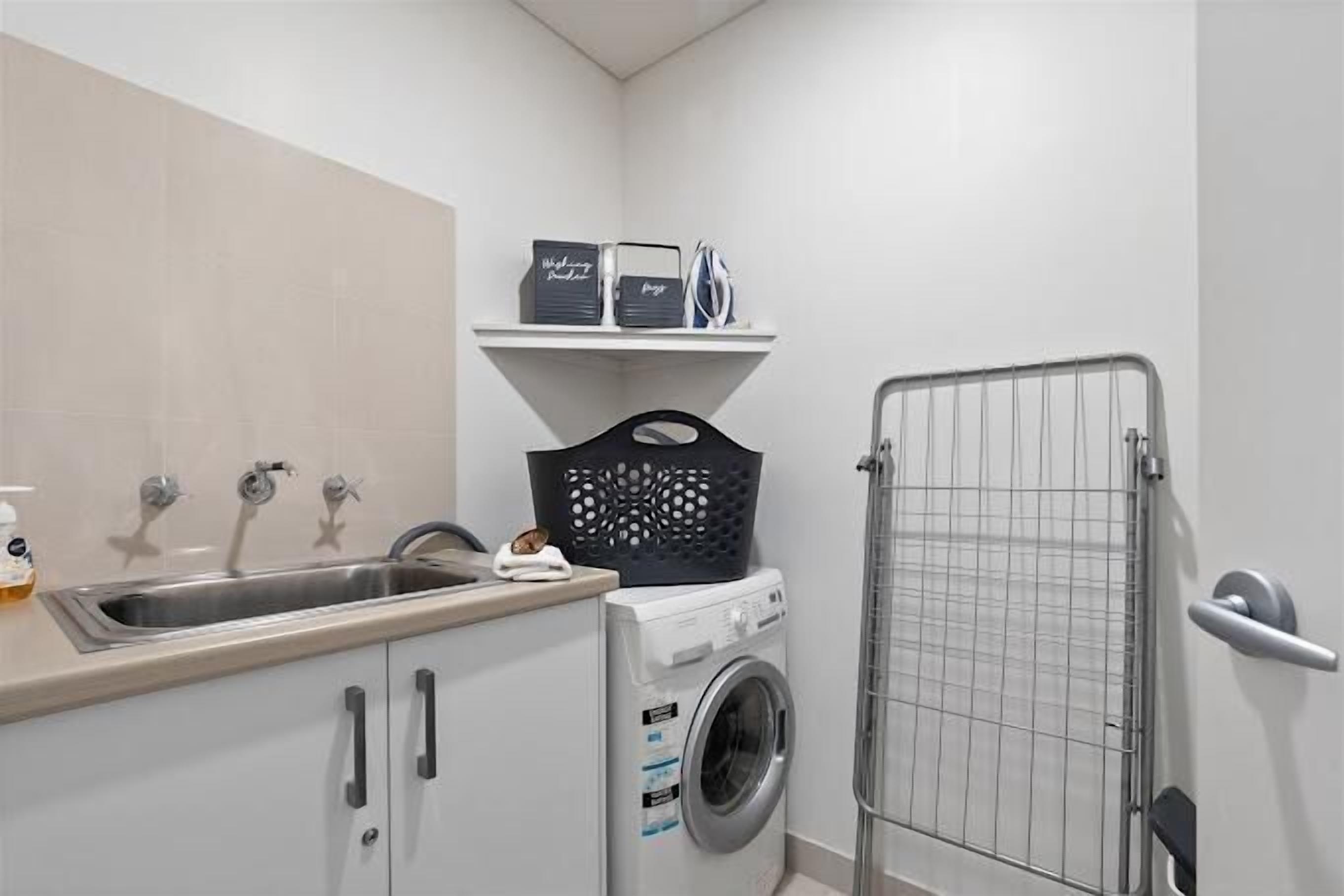 A compact laundry area with a washing machine, a sink, and a drying rack.
