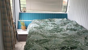 A bedroom with a bed, a window with blinds, a curtain, and a potted plant. - Converted French bus With Stunning Views (Beaworthy)