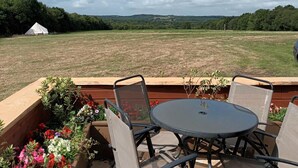 A patio with a round table and chairs, surrounded by a garden with various flowers. - Converted French bus With Stunning Views (Beaworthy)
