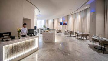 A hotel lobby with a reception desk, seating area, and a TV mounted on the wall.