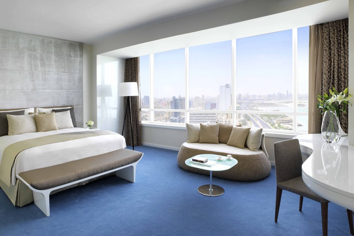 A modern hotel room with a large bed, a sofa, a small table, and a view of the city.