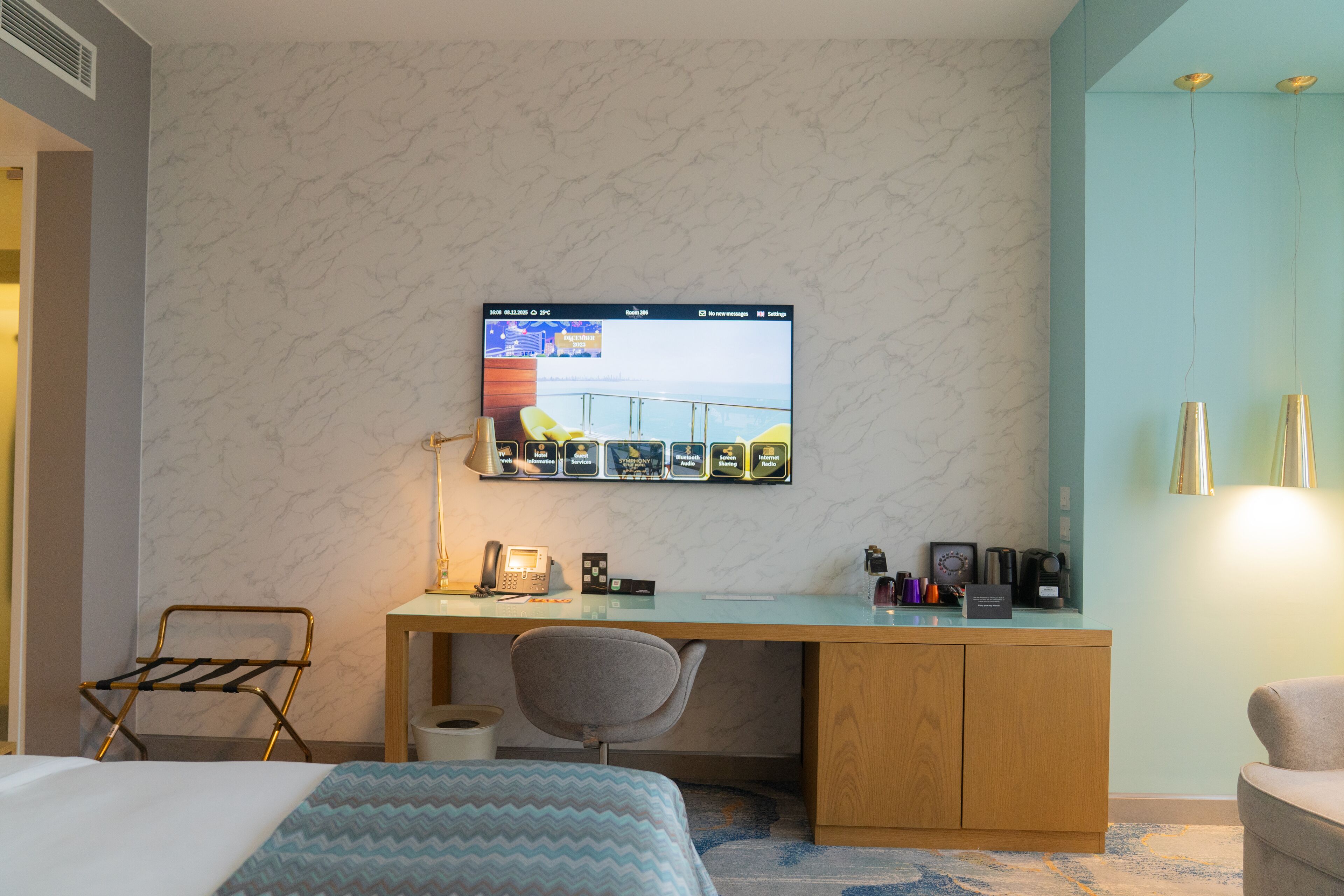 A hotel room with a bed, a desk with a computer, a chair, and a TV mounted on the wall.