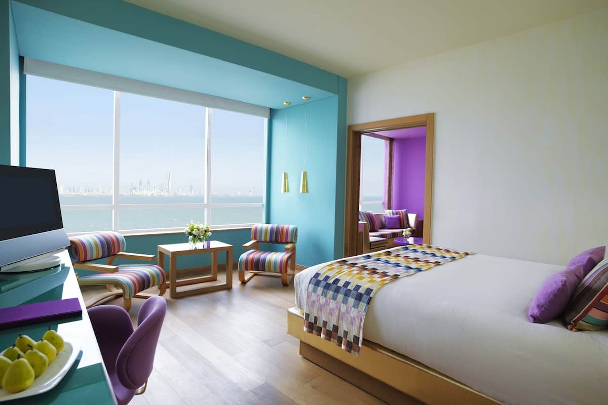 A modern hotel room with a large bed, a desk with a computer, and a view of the city skyline.