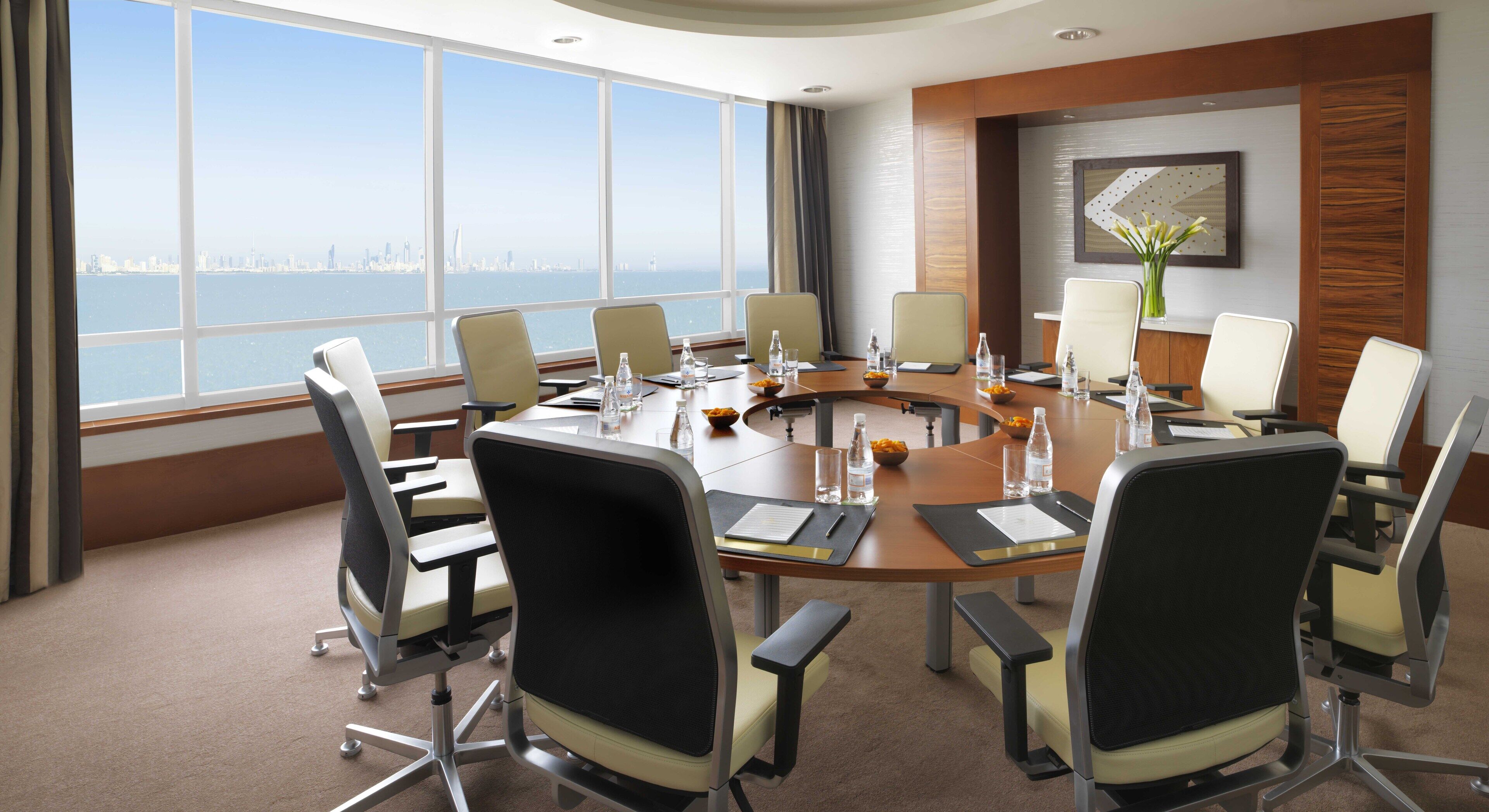 A conference room with a panoramic city view, modern furniture, and a large table with water bottles and documents.