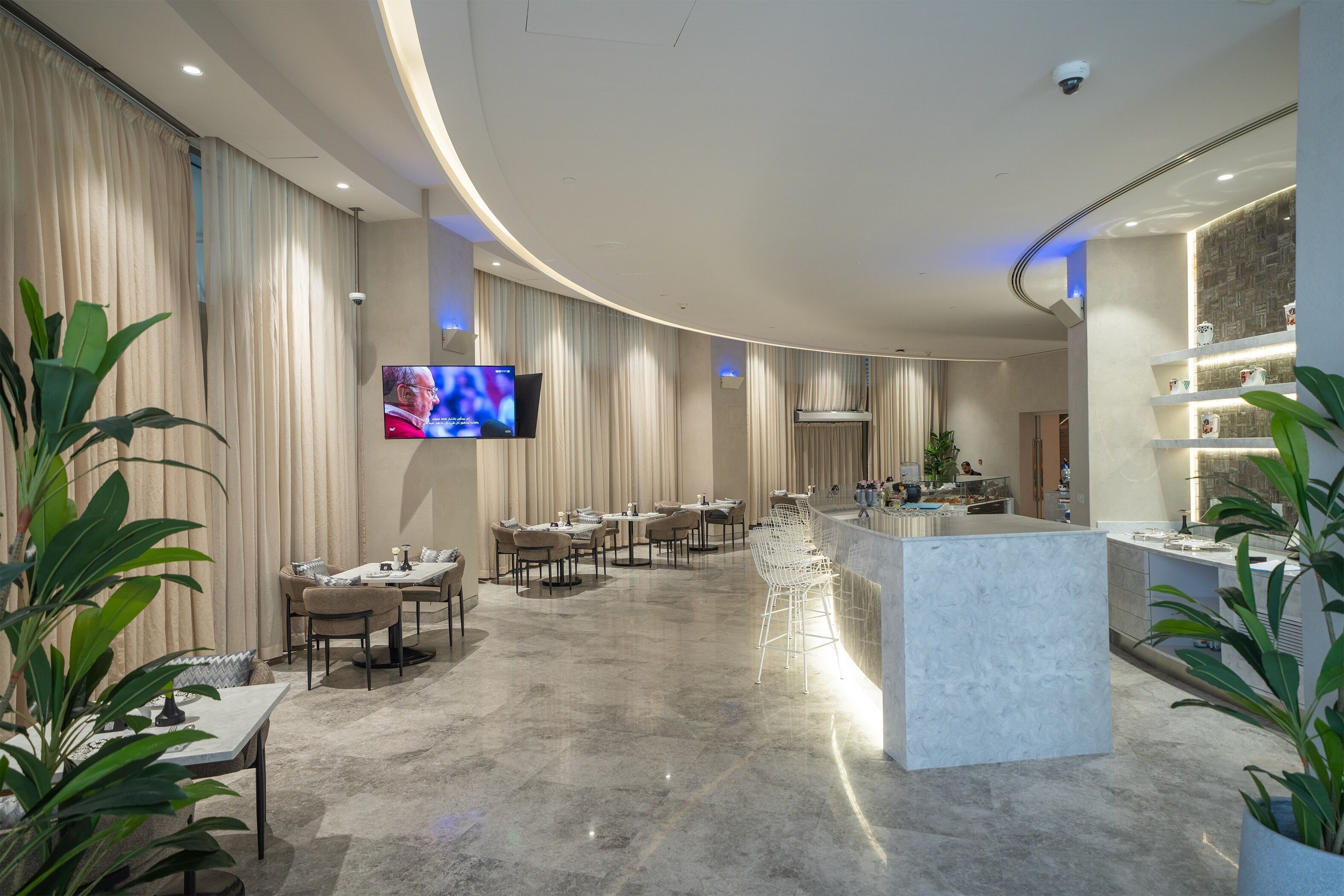 A modern hotel lobby with a curved ceiling, a central bar area, and a dining section with tables and chairs.