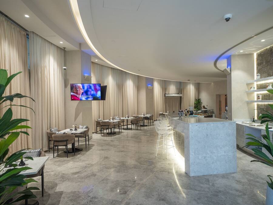 A modern hotel lobby with a curved ceiling, a central bar area, and a dining section with tables and chairs.