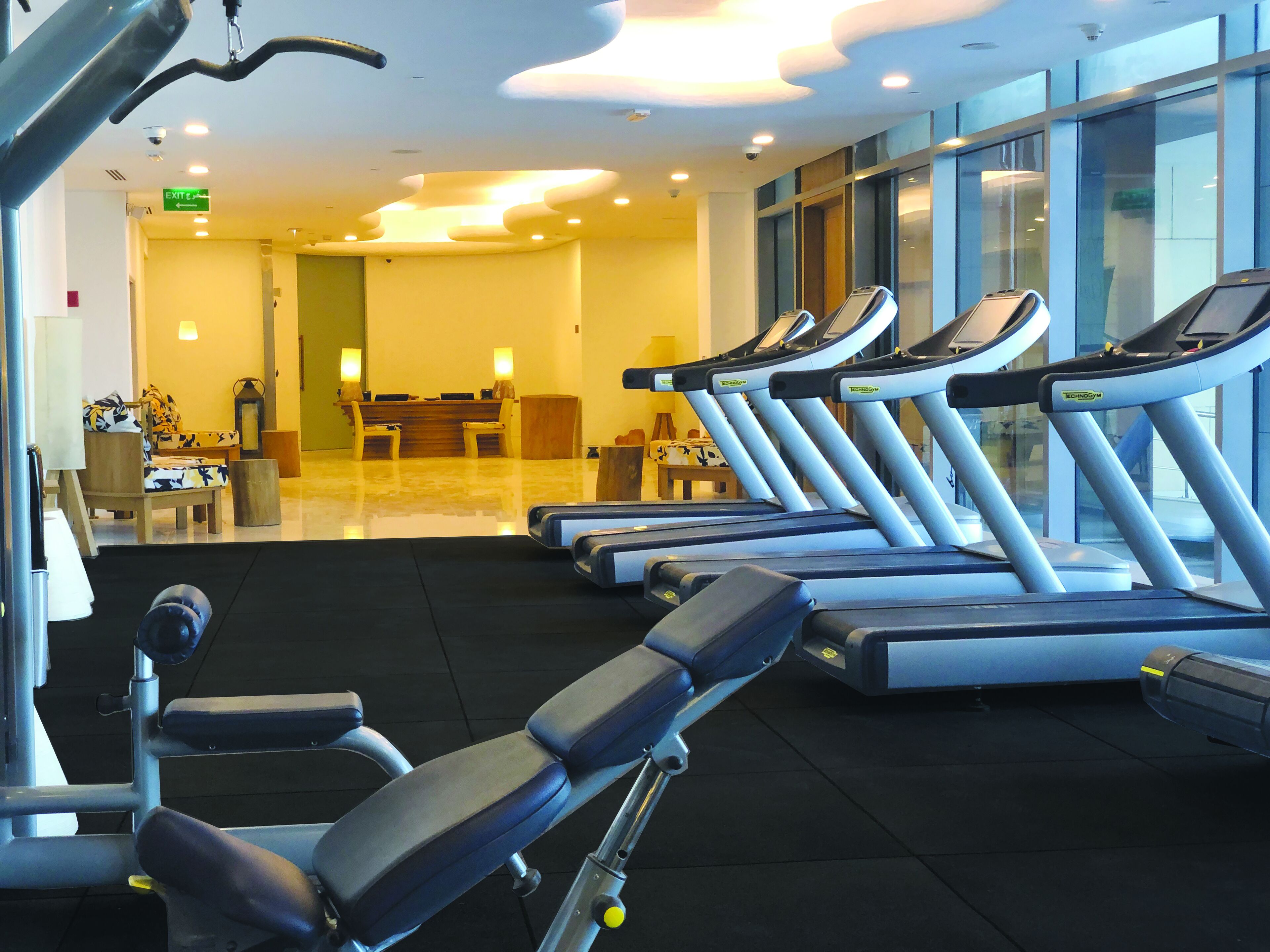 A gym with multiple treadmills, exercise equipment, and a reception area with chairs and a desk.