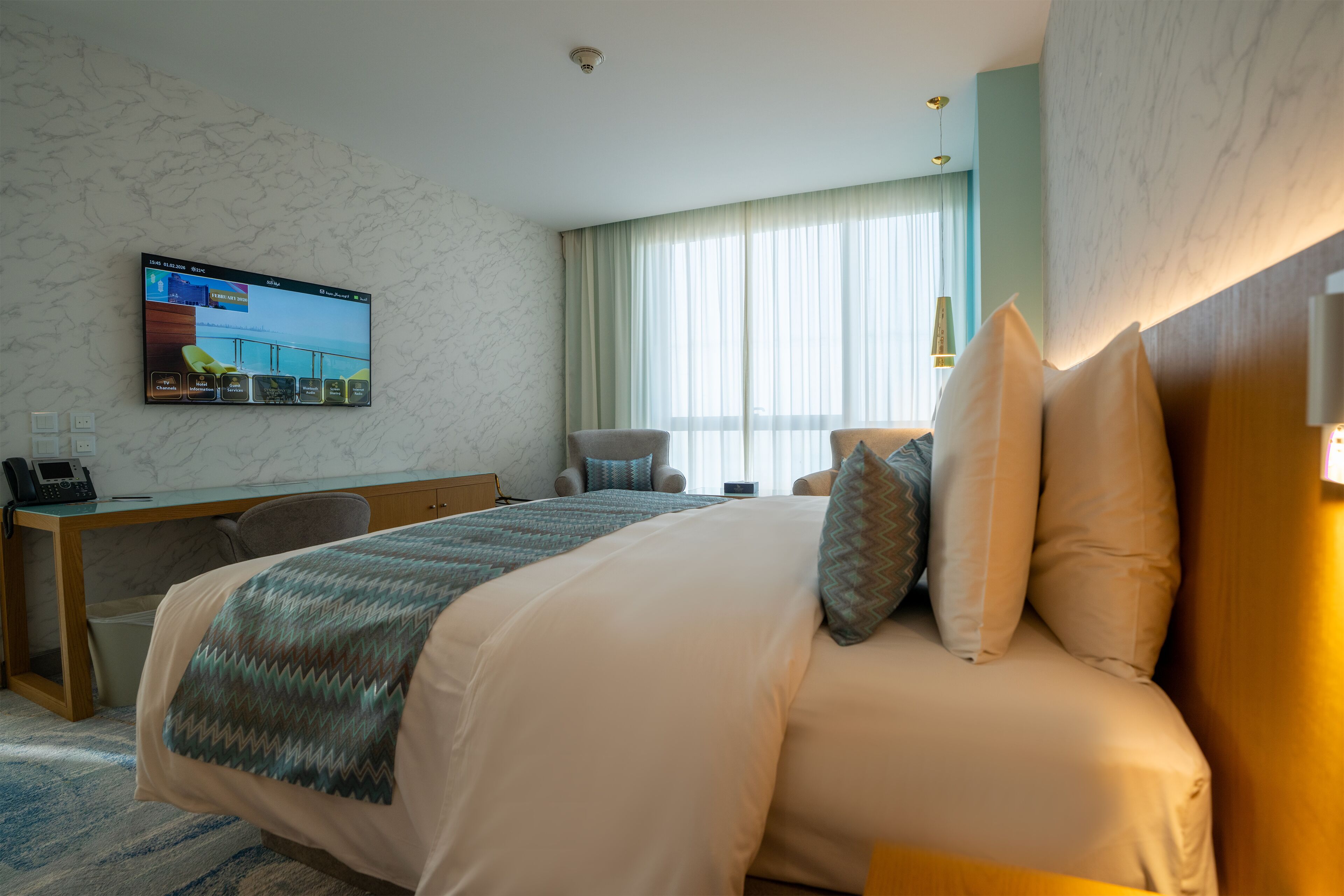 Een hotelkamer met een bed, een bureau, een stoel, een televisie aan de muur en een raam met gordijnen.
