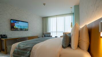 Een hotelkamer met een bed, een bureau, een stoel, een televisie aan de muur en een raam met gordijnen.