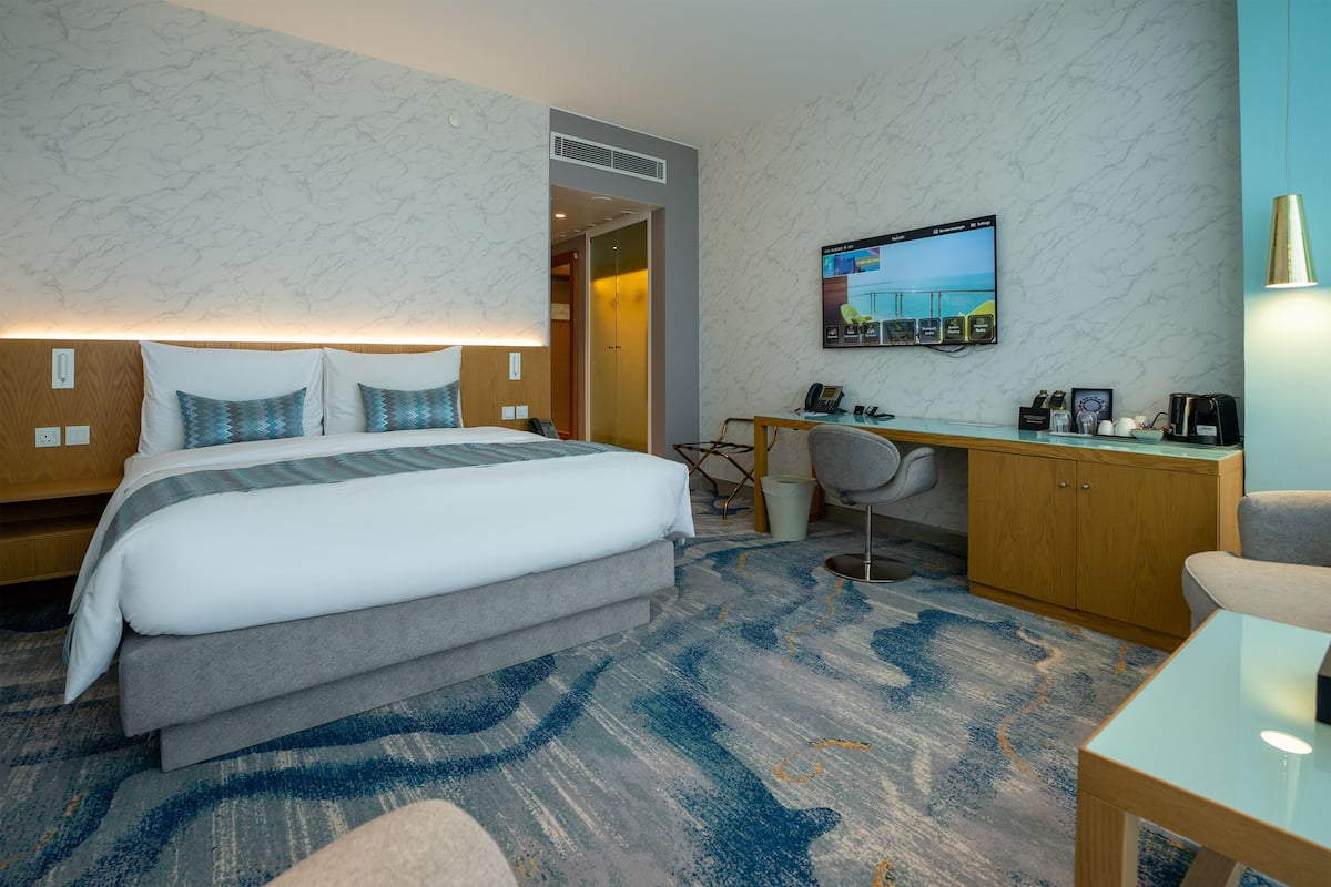 A hotel room with a bed, desk, chair, and a television mounted on the wall.