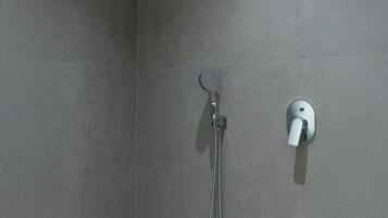 A shower area with a handheld showerhead and a wall-mounted control.