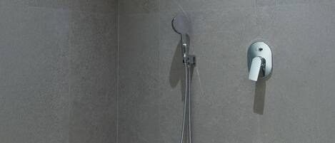 Un área de ducha con cabezal de ducha de mano y mandos en la pared.