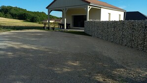A single-story building with a covered patio area, a stone wall, and a gravel driveway.