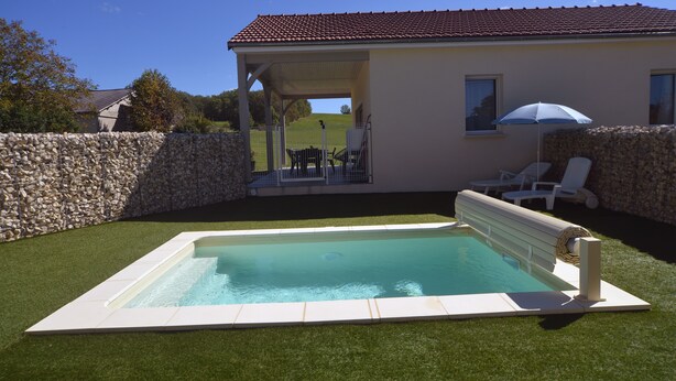 A swimming pool with a stone wall and a covered patio area with lounge chairs and an umbrella.