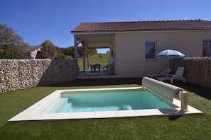 Ein Swimmingpool mit einer Steinmauer und einer überdachten Terrasse mit Liegestühlen und einem Sonnenschirm.