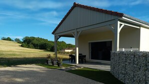 A covered patio area with a table and chairs, a stone wall, and a view of a grassy field.