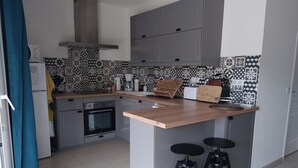 A compact kitchen with grey cabinets, a stainless steel oven, a coffee maker, and a small bar area with stools.