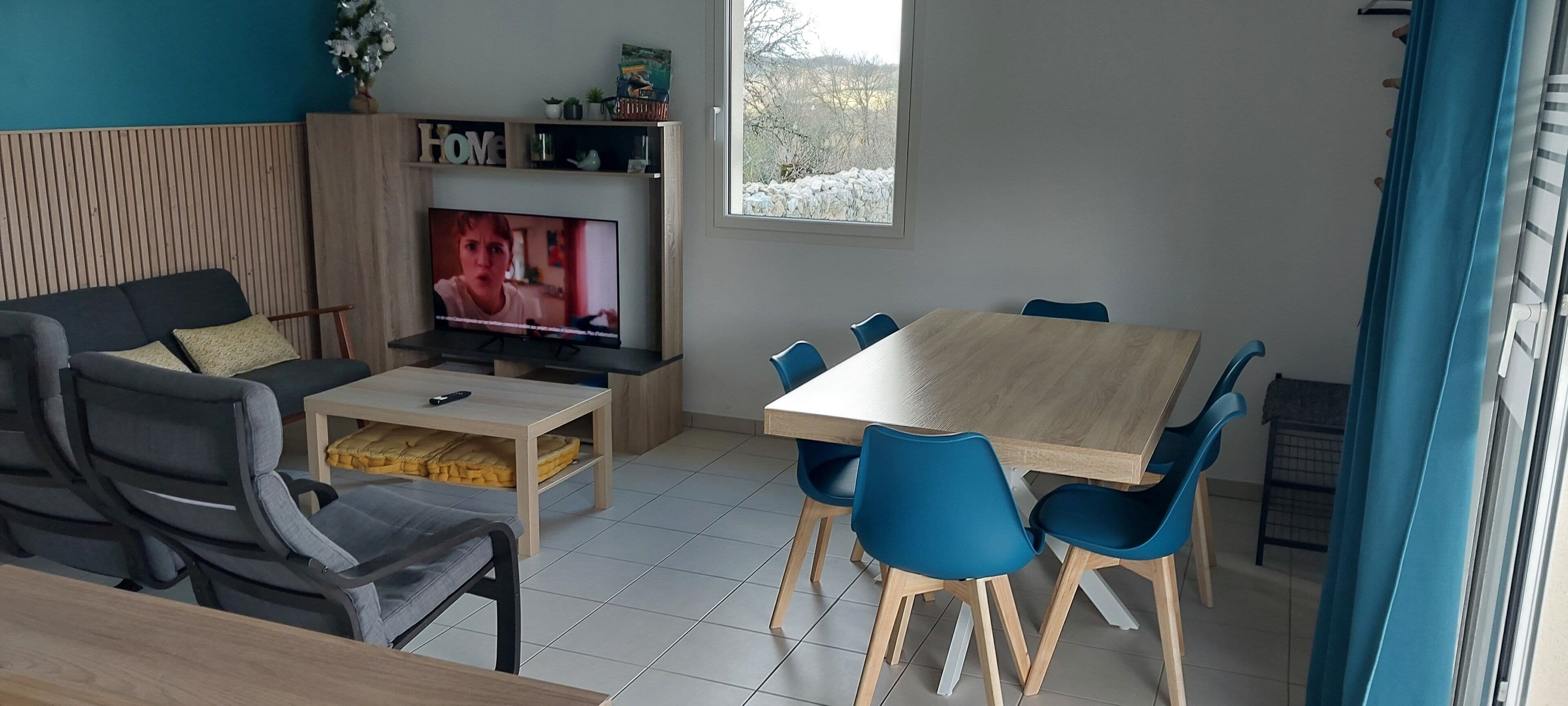 Een moderne woonkamer met een televisie, bank, salontafel en een eethoek met stoelen.