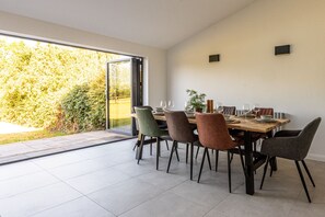 Un espace repas comprenant une grande table, plusieurs chaises et une vue sur la verdure grâce à une porte vitrée.