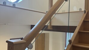 A wooden staircase with glass railings, a circular skylight, and a door with a fire extinguisher. - No1 Little Barrow Barns (Chester)