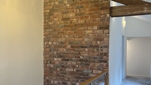 A staircase with a wooden handrail and glass balustrade, leading to a room with exposed brick walls and a hanging light fixture. - No1 Little Barrow Barns (Chester)