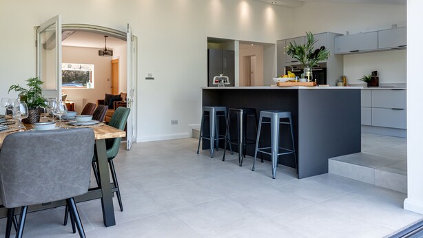 A modern kitchen with a central island, bar stools, and a dining area with a table set for six. - No1 Little Barrow Barns (Chester)
