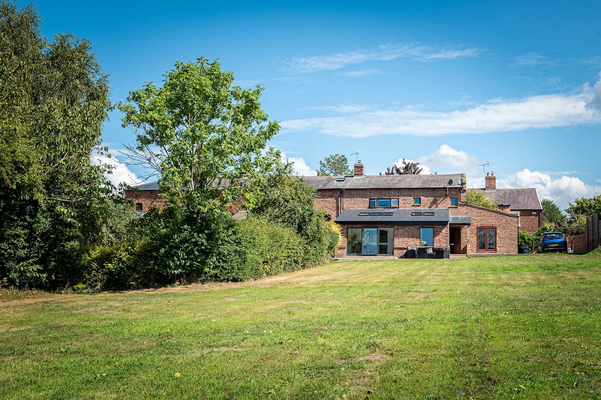 A two-story house with a brick exterior, a front lawn, and a blue car parked in the driveway.
