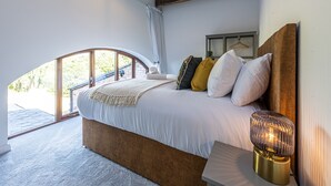 A bedroom with a large bed, a bedside table with a lamp, and a view of the outdoors through a large window. - No1 Little Barrow Barns (Chester)