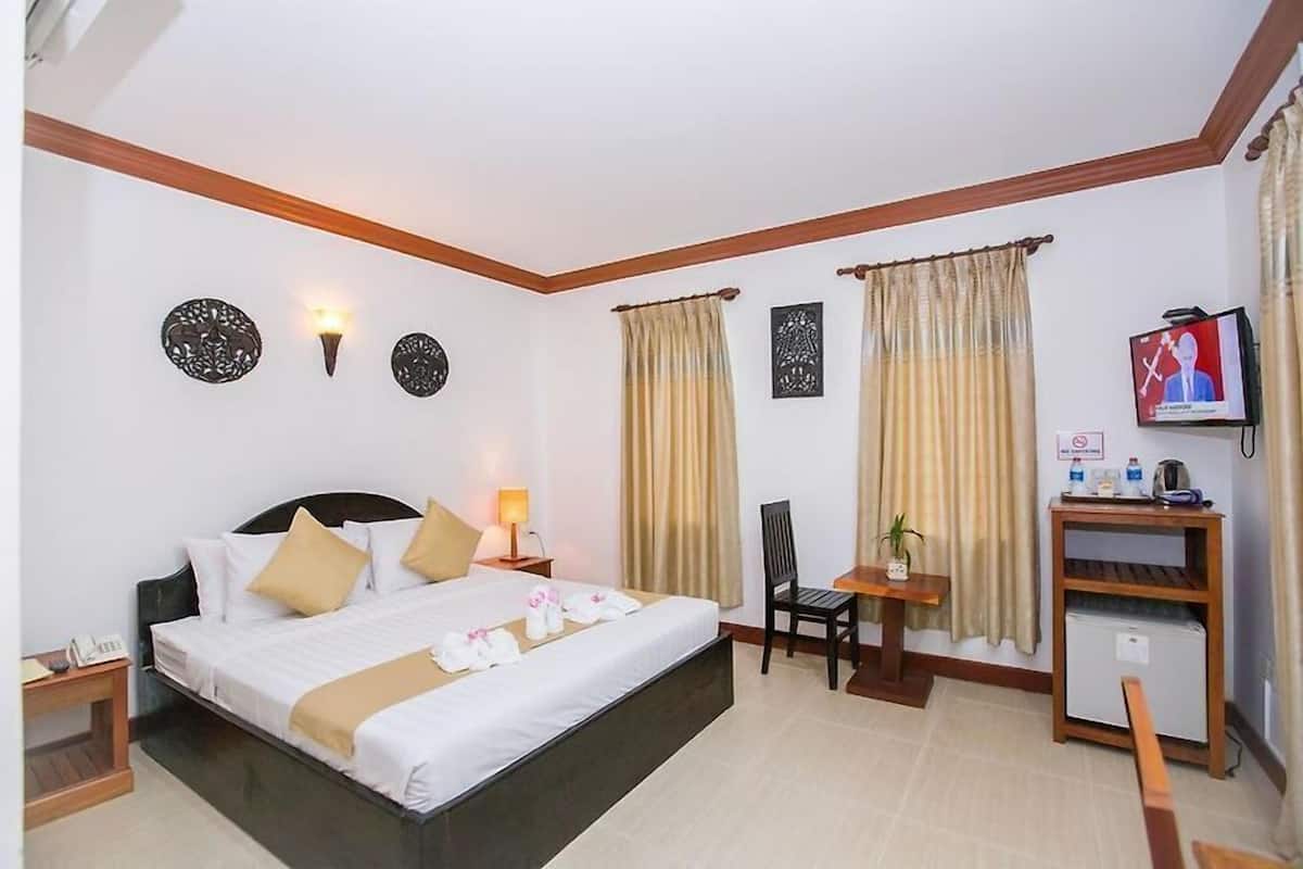 A hotel room with a bed, a desk, a chair, a TV, and a small table with a plant.