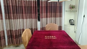 Un coin repas avec une table recouverte d’une nappe rouge, deux chaises et un rideau à motifs écossais.