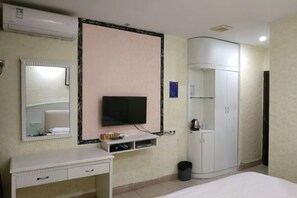 A hotel room with a bed, a TV mounted on the wall, a wardrobe, a small desk with drawers, and a trash bin. - Zhang Ying Hotel (Dongguan)