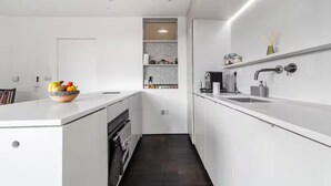A modern kitchen with white cabinetry, a central island, a built-in oven, and a dark wood floor. - Luxury Penthouse Near Notting Hill Gate | Stunning Sunset Views (London)