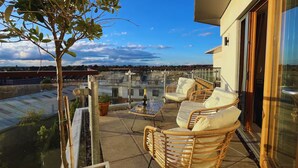 A balcony with wicker furniture, a small table with a bottle, and a potted plant. - Luxury Penthouse Near Notting Hill Gate | Stunning Sunset Views (London)