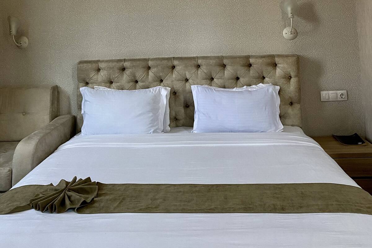 A hotel room with a large bed, two bedside tables, a headboard, and a wall-mounted light fixture.
