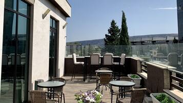 A rooftop terrace with outdoor seating, a glass balustrade, and a view of the cityscape.