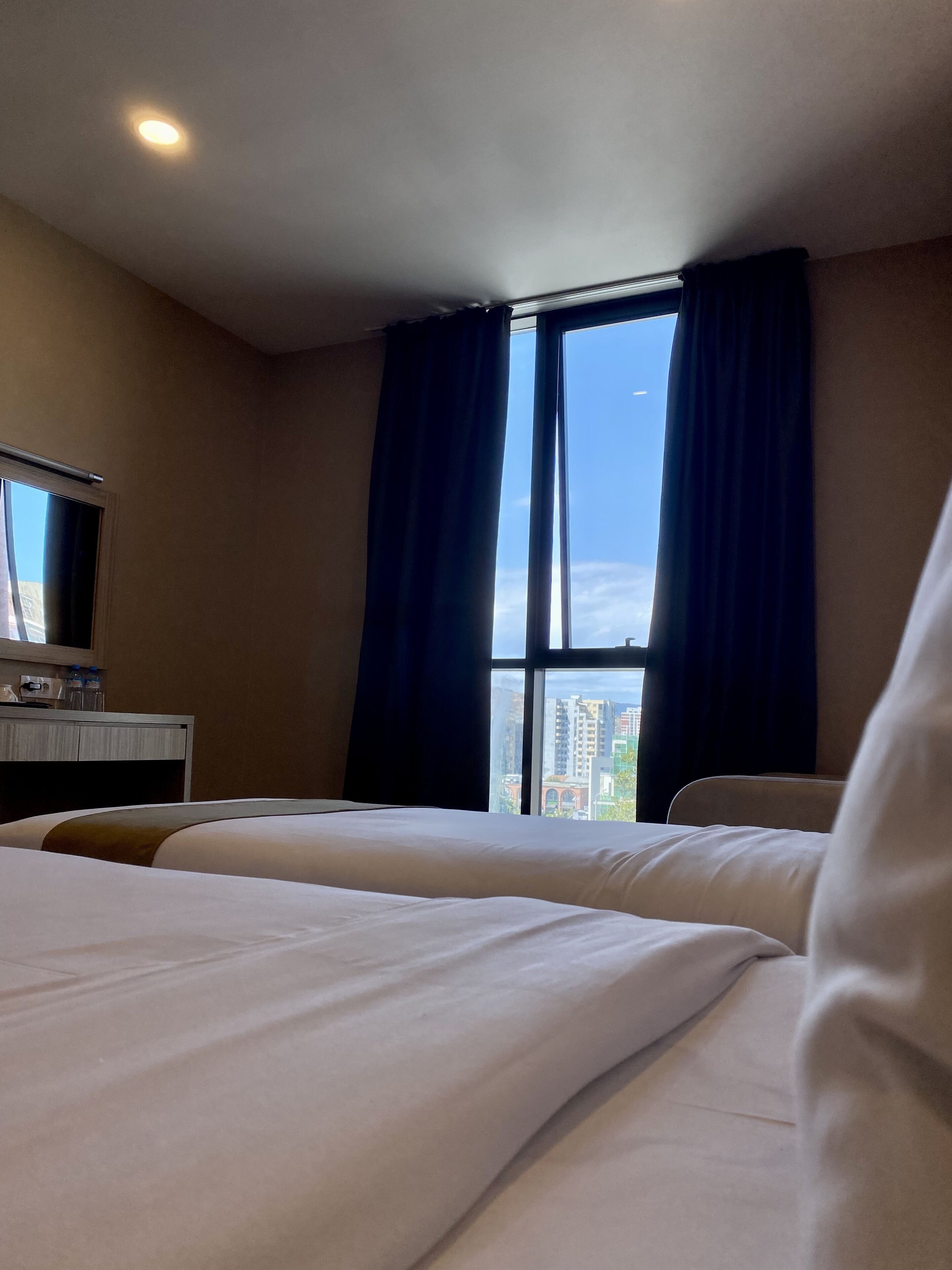 A hotel room with two beds, a desk with a mirror, and a window with curtains.