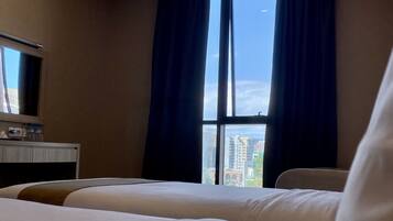 A hotel room with two beds, a desk with a mirror, and a window with curtains.