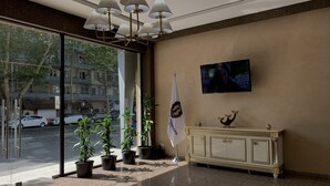 A lobby with a glass entrance, a television mounted on the wall, a flag, and a decorative cabinet. - Betlem Hotel (Tbilisi)