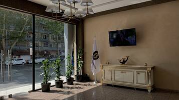 A lobby with a glass entrance, a television mounted on the wall, a flag, and a decorative cabinet.