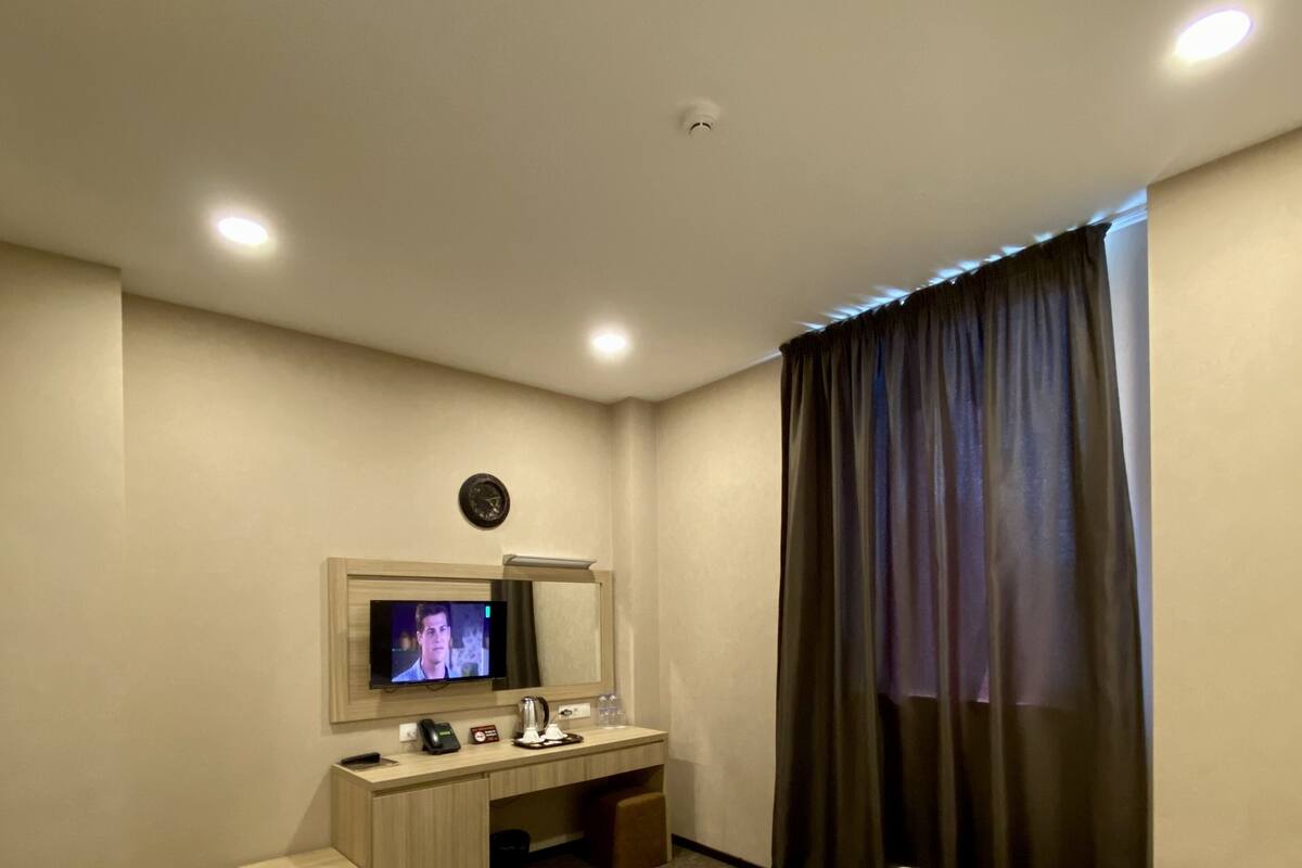 A hotel room with two beds, a desk with a mirror, a television, and a window with curtains.