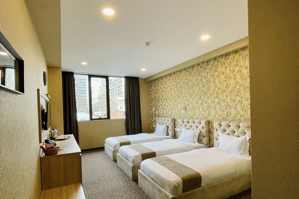 A hotel room with two beds, a desk, and a large window.