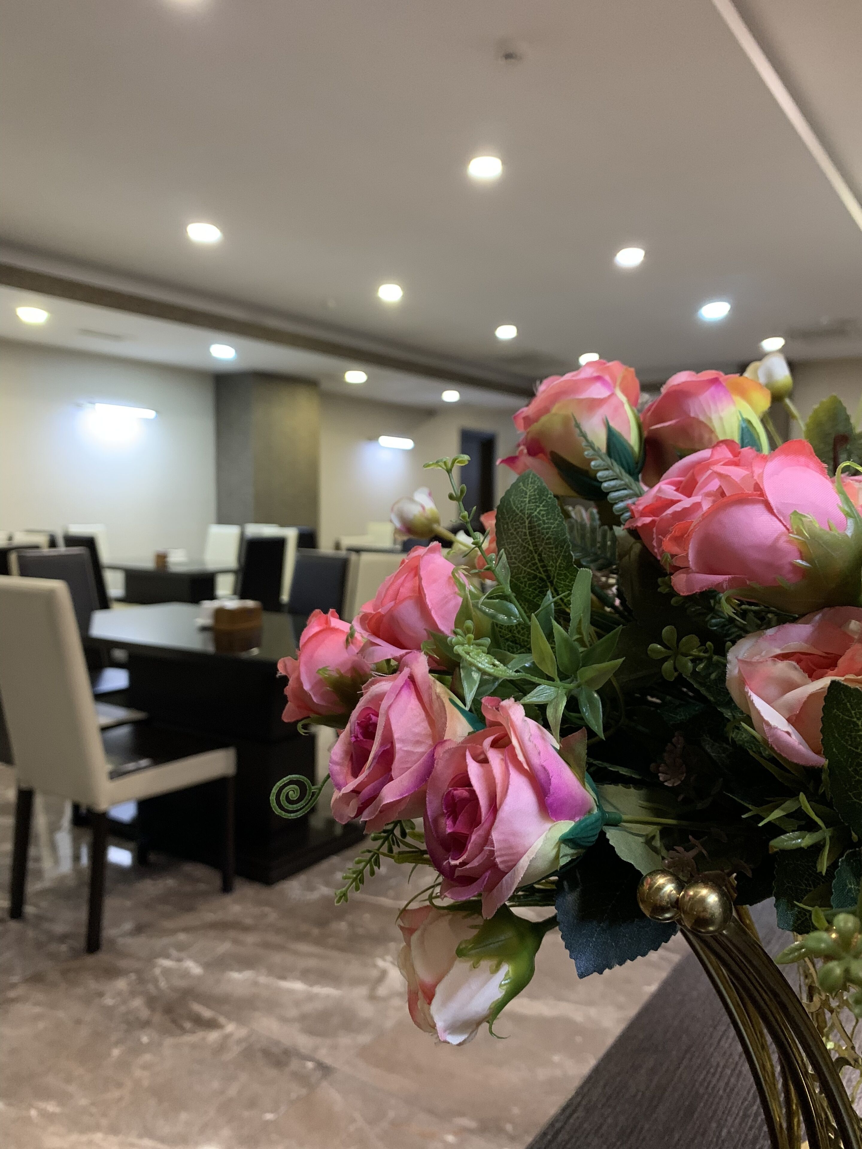 A conference room with a table and chairs, a floral arrangement on a table, and ceiling lights.