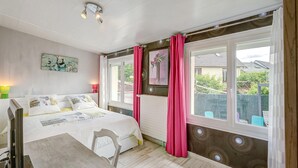Un dormitorio con cama, escritorio, silla, ventana con cortinas, radiador y un cuadro colgado en la pared.