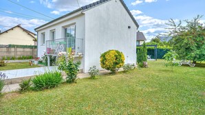 Una casa moderna de una sola planta con un pequeño jardín delantero, un balcón con plantas en macetas y un césped bien cuidado.