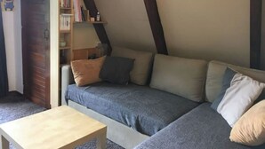 A cozy attic room with a built-in sofa, a wooden coffee table, and a bookshelf filled with books. - Chalet Guzet Snow (Seix)